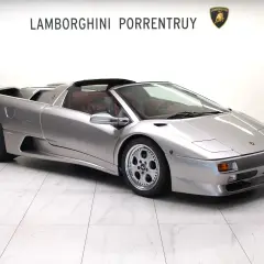 Srebrny kabriolet Lamborghini Diablo z czerwonym wnętrzem, zaparkowany na białej, marmurowej podłodze.
