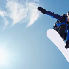 Snowboardzista w powietrzu, biała deska snowboard jak dobrać. Słońce i chmury na niebieskim tle.