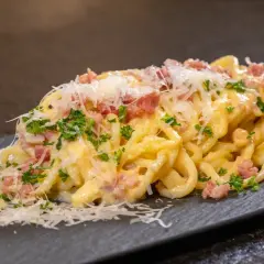 Eine Portion echte Carbonara mit cremiger Sauce, Guanciale und frisch geriebenem Parmesan auf einem dunklen Teller.