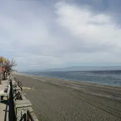 Un uomo corre sul lungomare di Roccafiorita, la spiaggia scura si estende verso l'orizzonte sotto un cielo nuvoloso.