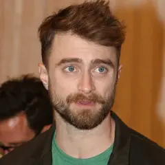 Daniel Radcliffe z zarostem i niebieskimi oczami, jego spojrzenie sugeruje troskę o zdrowie, być może związaną z jego chorobą.