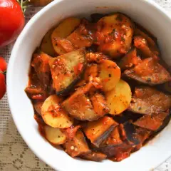 Pyszny adżapsandali przepis w misce, obok świeże pomidory. Warzywa duszone w sosie pomidorowym.