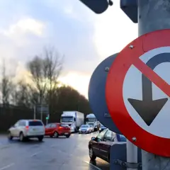 Znak zakaz zawracania na mokrej drodze, z samochodami w tle. Kierowcy muszą uważać, bo nie wolno tu zawracać.