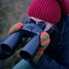 Dziewczyna w czerwonej czapce i rękawiczkach obserwuje niebo przez lornetkę Pentax. Idealna lornetka do obserwacji nieba.