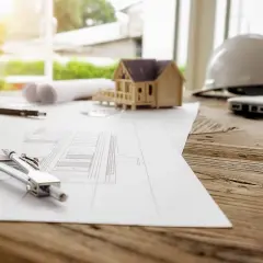 Na stole architekta leżą plany, model domu, cyrkiel i kask. Przygotowania do budowy, może potrzebny wzór zgody na wejście na działkę sąsiada.
