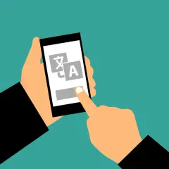 Dłoń trzyma smartfon z ikonami języków, a palec dotyka ekranu. Także czy tak że, tłumaczenie jest na wyciągnięcie ręki.