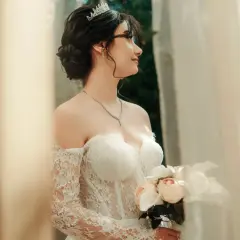 Eleganckie, najmodniejsze upięcia fryzury na wesele. Panna młoda w tiarze i sukni z koronki trzyma bukiet.