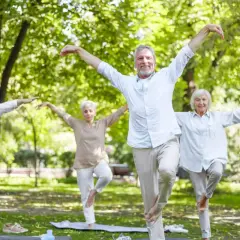 Senioren sport im Park: Vier ältere Menschen balancieren auf einem Bein, Arme ausgebreitet, in einer Yoga-ähnlichen Pose.