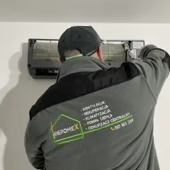 Technik w czapce z daszkiem montuje klimatyzator. Na kurtce logo firmy Higromex.