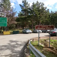Señal de "puerto de Navafría 1773 m" junto a señales de Castilla y León y Segovia. Coches aparcados en un día soleado.