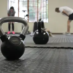Kettlebell 8kg na siłowni, w tle ćwiczący ludzie.