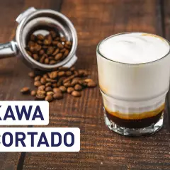 Kawa cortado z mleczną pianką, obok portafiltr z ziarnami kawy. Idealna na poranek.