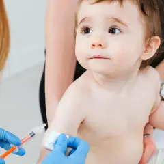 Małe dziecko otrzymuje szczepienie RSV. Ręka w niebieskiej rękawiczce trzyma strzykawkę, gotową do podania leku.