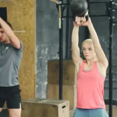 Uomo e donna eseguono esercizi con kettlebell, un allenamento completo per diversi gruppi muscolari in palestra.