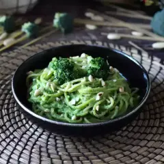 En skål med krämig broccoli pasta, toppad med broccolibuketter och hackade nötter. En härlig och grön måltid.