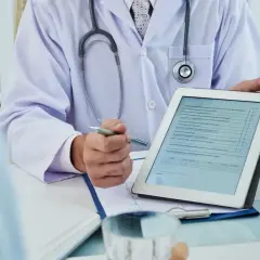 Medico con stetoscopio mostra un modulo su tablet, forse per una nuova unità di degenza.
