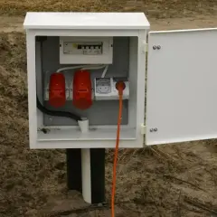 Skrzynka elektryczna na działce bez domu, z bezpiecznikami i gniazdami, gotowa na podłączenie prądu.