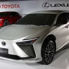 Elegancki, srebrny Lexus RZ prezentuje się na tle logo Toyoty i Lexusa.