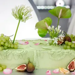 Elegancki tort ślubny w pastelowej zieleni, ozdobiony winogronami, figami i białymi kwiatami.