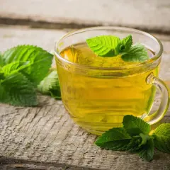 Une tasse de thé à la menthe, aux vertus et méfaits discutés, sur fond de bois vieilli.