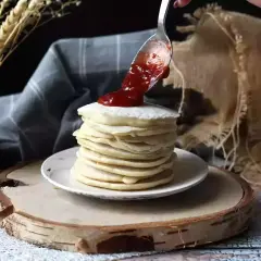 Una cuchara vierte mermelada sobre una pila de tortitas veganas.