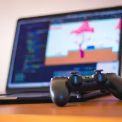 Kontroler PS4 leży przed laptopem z kodem i grą. Dowiedz się, jak podłączyć PS4 do laptopa, by grać na większym ekranie.