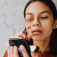 Ragazza usa un piegaciglia dorato, sperando che non rovina le ciglia.