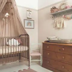 A serene modern nursery theme with a gold crib, cloud mobile, and rainbow art. A vintage dresser holds a woven basket, completing the cozy, dreamy atmosphere.