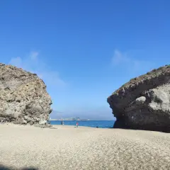 Dos rocas gigantes flanquean una playa de guijarros en la carbonera de Almería, con el mar azul y el cielo despejado de fondo.