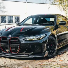 Czarny BMW M4 CSL z czerwonymi akcentami i sportowym dyfuzorem, zaparkowany na bruku.