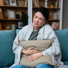 Donna sul divano con cuscino, dolori addominali e crampi, sintomi di diarrea dopo i pasti.