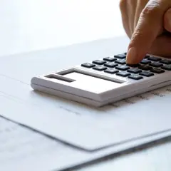 Dłoń naciska klawisze kalkulatora na papierze z liczbami. Zastanawiasz się, czy można połączyć kredyt gotówkowy z hipotecznym?