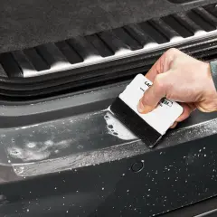 Mit der Rakeltechnik Anleitung wird die Folie blasenfrei angebracht. Ein weißer Rakel mit schwarzem Filzrand gleitet über die nasse Oberfläche des Autos.