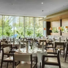 Elegancka sala restauracyjna Grand Hotel Tiffi w Iławie, z widokiem na zieleń. Stoły nakryte do posiłku, gotowe na przyjęcie gości.