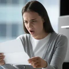 Zaskoczona kobieta czyta dokument. Czy pracodawca może zmusić do urlopu? Jej mina sugeruje, że to nie jest dobra wiadomość.