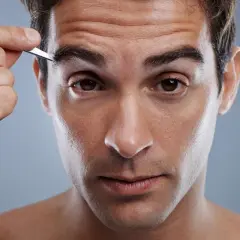 Uomo si sistema le sopracciglia con una pinzetta, cura del viso maschile.