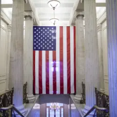 Wielka flaga USA wisi między marmurowymi kolumnami. Czy USA to stany zjednoczone? Tak, to symbol tego kraju.