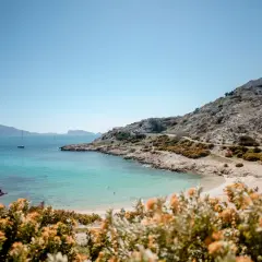 Vue panoramique d'une crique aux eaux turquoise sur la plage frioul, avec des voiliers au loin et des collines rocheuses.
