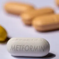 Eine weiße Tablette mit der Aufschrift "Metformin" liegt im Vordergrund. Im Hintergrund sind unscharfe gelbe und orangefarbene Pillen zu sehen. Forschung untersucht, ob Metformin bei Demenz helfen kann.
