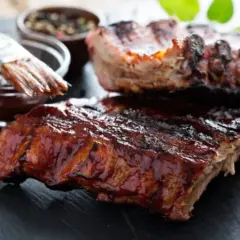 Saftige Rippchen, glasiert mit BBQ-Sauce. Ein Pinsel taucht in die Sauce, bereit für die Zubereitung: low and slow.