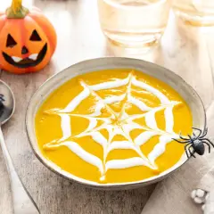 Soupe de citrouille décorée d'une toile d'araignée en crème, avec une citrouille d'Halloween et des araignées.