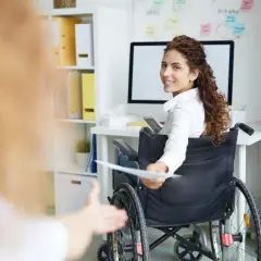 Donna in carrozzina sorride, porgendo documenti. La legge 68/99 offre vantaggi per il lavoratore, promuovendo inclusione e pari opportunità.