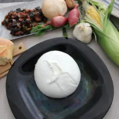 Mozzarella di bufala salernitana su piatto nero, con pane, verdure e mais.