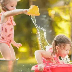 Bambine felici si divertono con giochi d'acqua sotto il sole estivo, spruzzandosi a vicenda con secchielli e bacinelle.