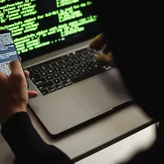 Un développeur web, définition : une personne manipulant du code sur un smartphone et un ordinateur portable, éclairés par la lueur verte des écrans.