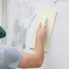 Pracownik w masce wygładza ścianę pacą. Ciekawi Cię, ile schnie tynk mozaikowy?