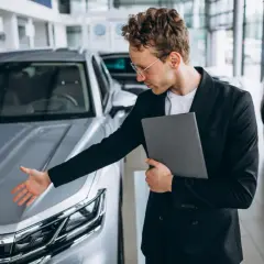 Mężczyzna w garniturze prezentuje samochód, oferując leasing dla nowych firm.