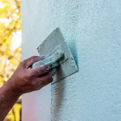 Dłoń zacierająca tynk na ścianie za pomocą kielni. Powstaje faktura rajberka.