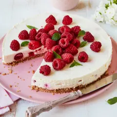 Eine köstliche Philadelphia Torte Himbeer, üppig garniert mit frischen Himbeeren und Minze, auf einem rosa Teller.