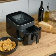 Chrupiące chipsy z airfryera w misce obok urządzenia. Na desce ser, oliwa, wino i kieliszki.